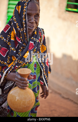 Une vieille femme Peul dans la région de la ville de Djibo dans le nord du Burkina Faso, secoue une calebasse de lait frais. Banque D'Images