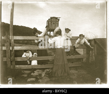 Des femmes fortes ascenseur baby carriage par dessus la clôture qui revient de la foire. c. 1900 robe victorienne Banque D'Images