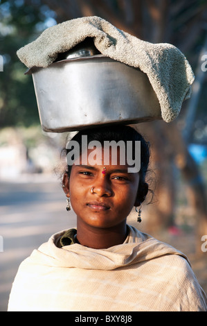 Les Indiens de la caste inférieure pauvre adolescente Porter une casserole de riz sur la tête. L'Andhra Pradesh, Inde Banque D'Images