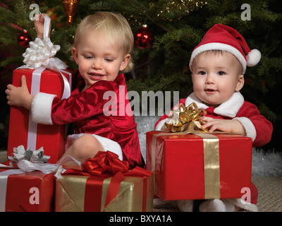 Fillette de deux ans et un garçon de huit mois ouvrant leurs cadeaux sous un arbre de Noël Banque D'Images