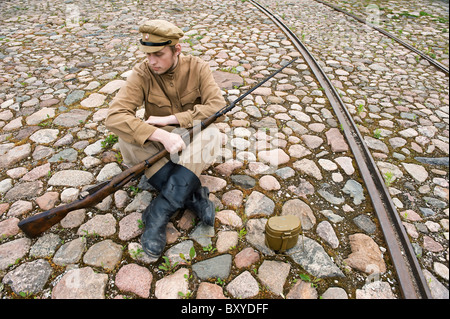 Soldat avec l'arme et de chaudière en uniforme de la Première Guerre mondiale, s'asseoir et se reposer sur la chaussée. Les temps de l'accord de costume World W Banque D'Images