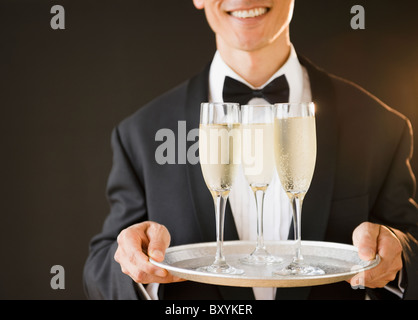 Le port de serveur et Bow-tie holding tray with champagne flutes, studio shot Banque D'Images