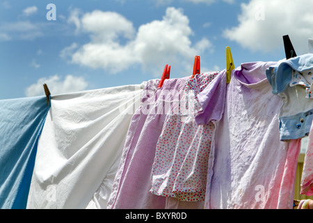 Les vêtements pour enfants et les draps ont été accrochés à sécher sur une corde à vue contre un ciel bleu avec des nuages. Banque D'Images