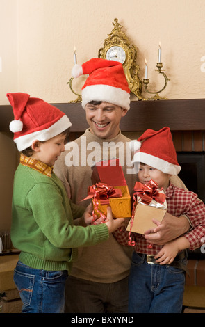 Portrait de père et ses fils wearing santa hats avec présente dans les mains Banque D'Images