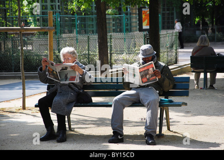 Les personnes lisant le journal sur banc de parc Paris France Banque D'Images