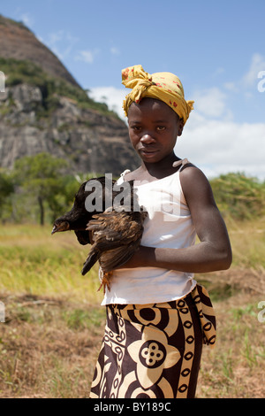 MECEBURI, près de Nampula, MOZAMBIQUE, Mai 2010 : Une jeune fille est titulaire d'un chichen pendant que son père corrige sa moto. Banque D'Images