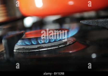 Close-up of blue les flammes brûler sur une cuisinière vitrocéramique avec un pan d'orange à l'arrière du terrain Banque D'Images