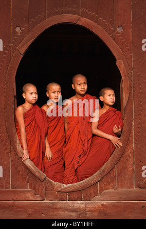 Le Myanmar, Birmanie, Nyaungshwe. Les jeunes moines novices debout à une fenêtre ovale en bois, Shwe Yaunghwe Kyaung monastère. Banque D'Images