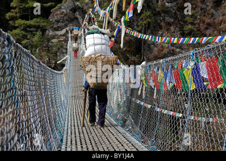 Le Népal, Everest, Région de la vallée de Khumbu. Porteurs lourdement chargés traverser le pont suspendu sur le fil sur le camp de base de l'Everest Trek près de Banque D'Images