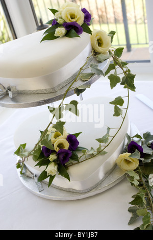 Gâteau de mariage blanc à deux vitesses drapé de pourpre et fleurs crème de lierre Banque D'Images