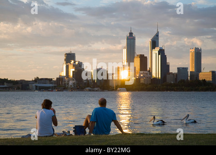 L'Australie, Western Australia, Perth, Perth Sud. Un couple regarder de l'autre côté de la rivière Swan à l'horizon de la ville au crépuscule. Banque D'Images