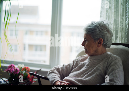 Vieille Femme assise en chaise à la recherche sur les fleurs. Banque D'Images