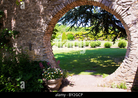 Une ouverture circulaire dans le mur d'un jardin d'été Anglais en vue de la pelouse paysagée et au-delà de topiaires Banque D'Images