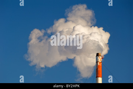 Fumée, gaz et de la vapeur s'élève de une cheminée contre un ciel bleu. Banque D'Images