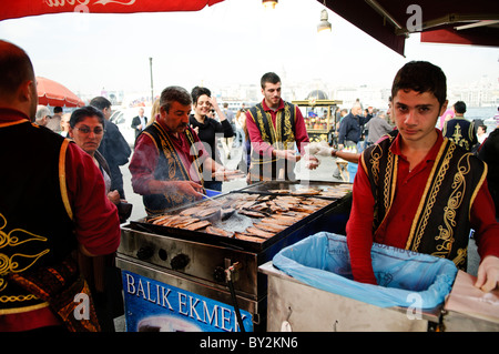 Balik Ekmek Fish Sandwich Street Food Istanbul Turquie // ISTANBUL, Turquie — Un vendeur de rue grillera du poisson frais sur le front de mer d'Eminonu, près du pont de Galata, préparant le traditionnel balik ekmek (sandwich au poisson). Le balik ekmek, généralement préparé avec du maquereau grillé servi dans du pain blanc avec des oignons et de la laitue, est l'un des plats de rue les plus populaires d'Istanbul. Les vendeurs de poissons riverains opèrent à partir de bateaux flottants et de stands le long de la Corne d'Or à cet endroit depuis des générations. Le quartier d'Eminonu sert de terminal de ferry majeur et de plaque tournante commerciale reliant l'Europe et l'Asie d'Istanbul Banque D'Images