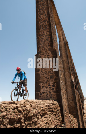 Un homme chevauche son vélo sous un grand aqueduc au cours d'une excursion à bicyclette à travers les haciendas Pulqueras Ex de l'état de Hidalgo, au Mexique. Banque D'Images