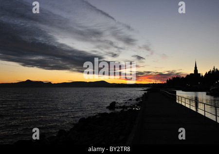 Silhouette vue de la plage, avec le clocher de la cathédrale, de l'aube rouge ciel au-dessus de montagnes, Lac Nahuel Huapi, Bariloche, Argentine Banque D'Images