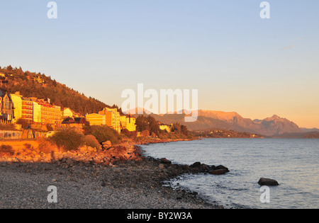 Tôt le matin soleil sur plage au bord du lac, les bâtiments de l'hôtel Lac Nahuel Huapi et Cerro Lopez Andes peaks, Bariloche, Argentine Banque D'Images