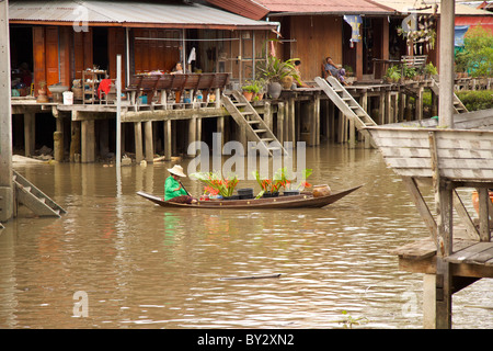 Marchande de fleurs portant une veste verte la vente de bouquets de graines Ptychosperma microcarpum à partir d'un bateau sur le canal au marché flottant d'Amphawa Banque D'Images