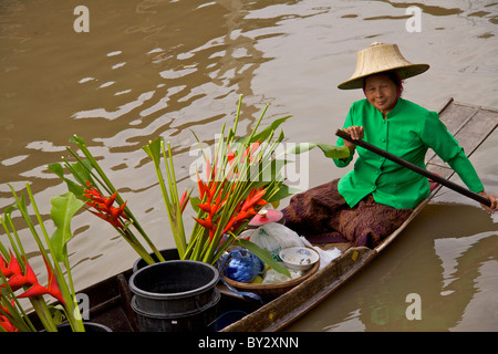 Marchande de fleurs portant une veste verte la vente de bouquets de graines Ptychosperma microcarpum à partir d'un bateau sur le canal au marché flottant d'Amphawa Banque D'Images