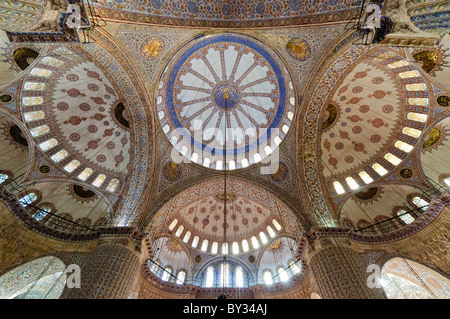 Mosquée Bleue 17e siècle Décoration intérieure ottomane de la coupole Istanbul Turquie | ISTANBUL, Turquie — La coupole centrale de la mosquée Sultan Ahmed, communément appelée la Mosquée Bleue, présente les demi-coupoles en cascade et les ornements peints typiques de l'architecture religieuse ottomane classique. Commandée par le Sultan Ahmed I et achevée en 1616, le bâtiment a été conçu par l'architecte impérial en chef Sedefkâr Mehmed Ağa selon un plan en quatre-feuilles dérivé de la mosquée Şehzade de Mimar Sinan. Ses surfaces intérieures comportent plus de 21 000 tuiles İznik et Kütahya ainsi que des calligraphies de Seyyid Kasım Gubari. Banque D'Images