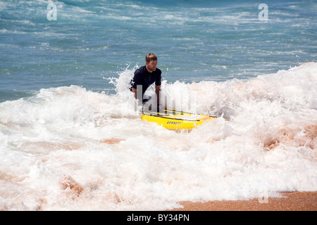 Homme à genoux sur une planche de surf jaune s'approche de la plage, sur une vague Banque D'Images