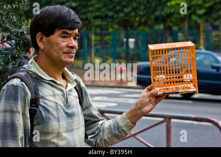 Homme avec petit oiseau en cage orange dans le marché aux oiseaux, Yuen Po Street, Nathan Road, Kowloon, Hong Kong. JMH4145 Banque D'Images