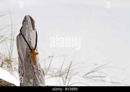 Cross est suspendu par un collier de corde tressée sur un morceau de bois flotté avec une superbe plage. Banque D'Images