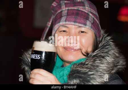 Une asiatique femme boit une pinte de Guinness dans un pub irlandais à Limerick, en Irlande. Banque D'Images