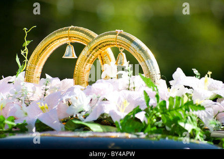 Close-up de gros anneaux d'or de mariage avec des cloches par fleurs blanches sur toit de voiture Banque D'Images