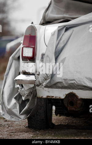 Un vieux classique MG voiture blanche couverts et prêt à être réparés comme un projet de restauration Banque D'Images