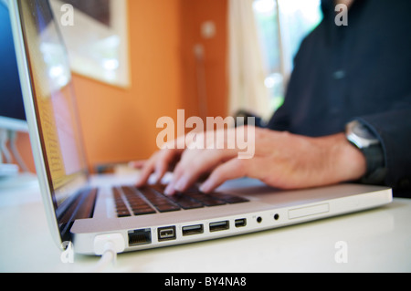 Homme assis derrière un ordinateur portable à un bureau d'écrire un texte. Banque D'Images