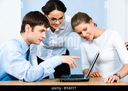Portrait of serious businessman assis à la table et pointant vers le moniteur portable avec deux dames en souriant près de Banque D'Images