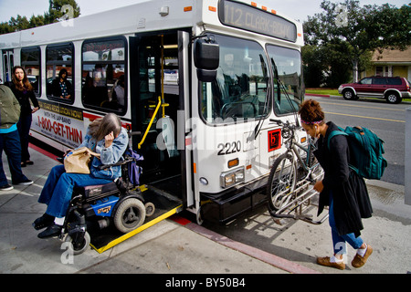 Un collège communautaire handicapés étudiant dans un fauteuil roulant motorisé à bord d'un bus de ville à l'aide d'une rampe repliable à Long Beach, CA, Banque D'Images