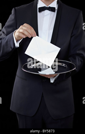 Portrait d'un homme vêtu d'un smoking et tenant une enveloppe au-dessus d'un plateau d'argent Banque D'Images