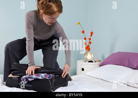 Une femme essayant de fermer une valise débordante Banque D'Images