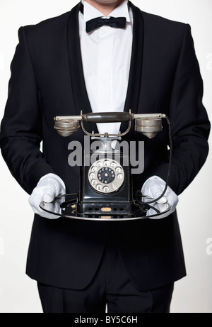 Un butler holding un ancien téléphone à cadran sur un plateau d'argent, side view Banque D'Images