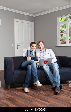 Un jeune couple à l'aide d'un ordinateur portable ensemble dans leur salle de séjour Banque D'Images
