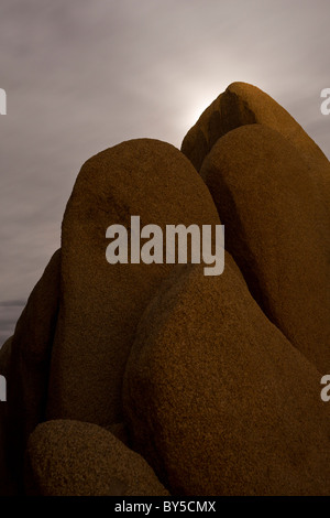 Lune de lumière venant de derrière de gros rochers de granit dans la nuit dans le parc national Joshua Tree, désert de Mojave, Californie, USA. Banque D'Images