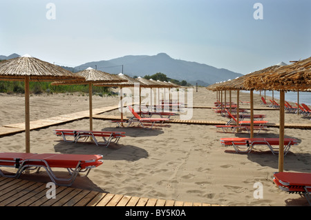 Des parasols de paille et des rangées de chaises de salon de bronzage à sandy beach en Grèce. Banque D'Images