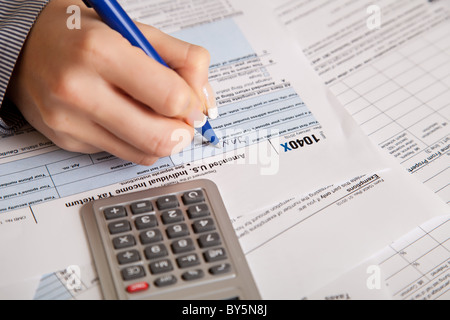 Main femme remplissant les formulaires d'impôt sur le revenu avec la calculatrice Banque D'Images