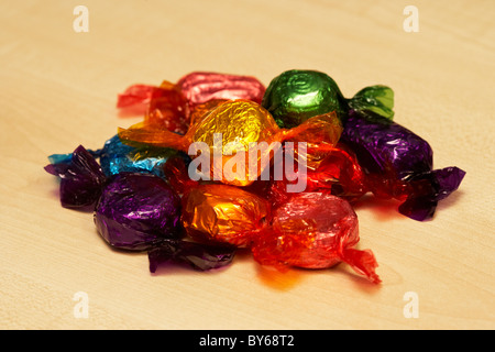 Tas de bonbons de chocolat enveloppé dans les emballages colorés sur une surface en bois Banque D'Images