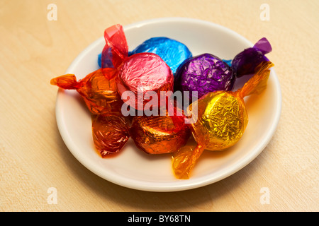 Tas de bonbons de chocolat enveloppé dans les wrappers colorés sur une petite plaque Banque D'Images