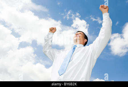 Portrait of happy businessman levant les mains avec ciel nuageux au-dessus de lui Banque D'Images