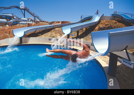 Jour de ciel bleu chaud au parc aquatique Algarve garçon adolescent ayant plaisir glissant hors de la chute d'eau à grande vitesse dans l'eau profonde au Portugal Banque D'Images