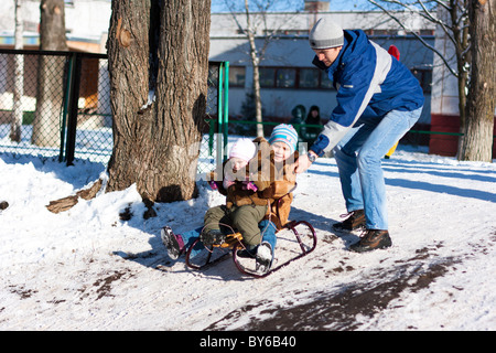 Père poussent les enfants en bas de la colline dans un traîneau en hiver en plein air Banque D'Images