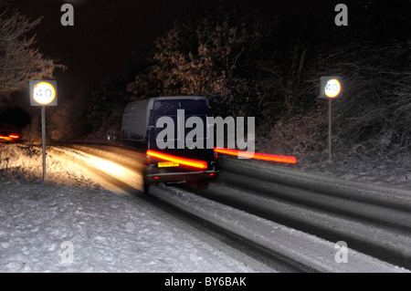 Conduite en minibus sur une route enneigée avec un véhicule de nuit dépassant le panneau de limite de vitesse de 40 km/h éclairé par une exposition au flash et des traces de lumière d'obturation lente Angleterre Royaume-Uni Banque D'Images