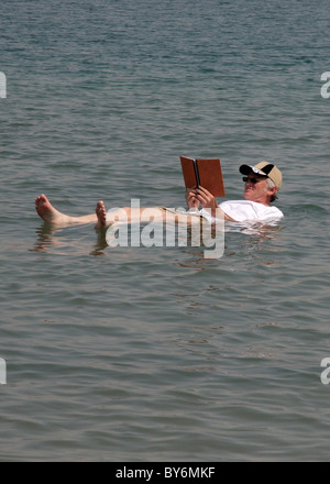 Un senior adulte lit un livre tout en flottant sur la mer Morte en Israël. La forte teneur en sel sans effort permet de flotter. Banque D'Images