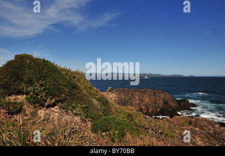 Ciel bleu sur les eaux bleues de l'océan Pacifique d'une vague de coupe plate-forme de basalte avec colline, Ile de Chiloé, Chili Banque D'Images