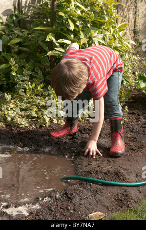 Garçon jouant avec le soutien de faire une flaque d'eau et de boue dans le jardin arrière. quatre-année-vieux Banque D'Images